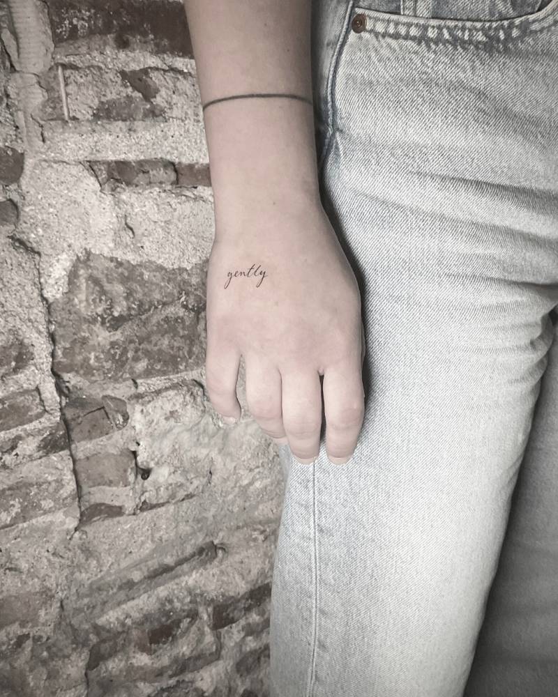 Script font word "gently" tattoo located on the hand.