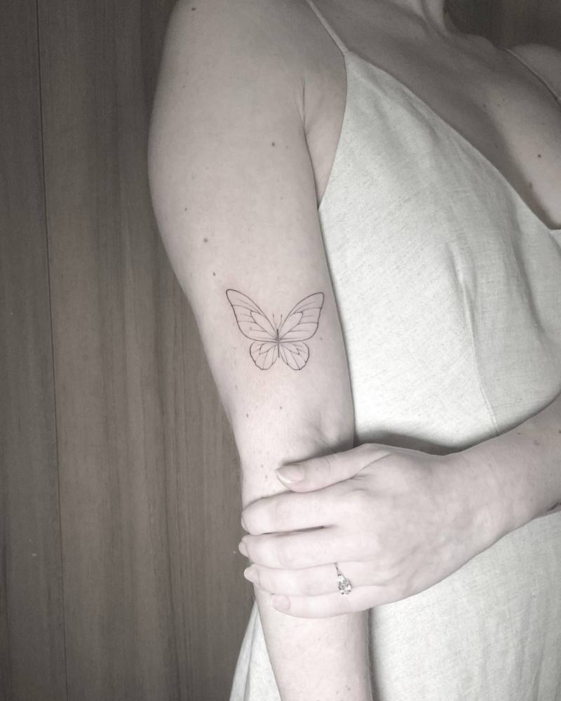 Fine line style butterfly tattoo located on the upper arm.