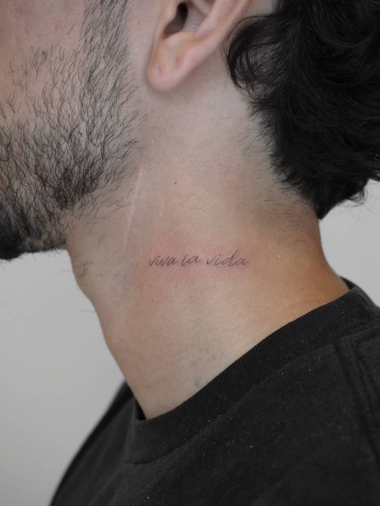 Handwritten font "viva la vida" lettering tattoo located on the neck.