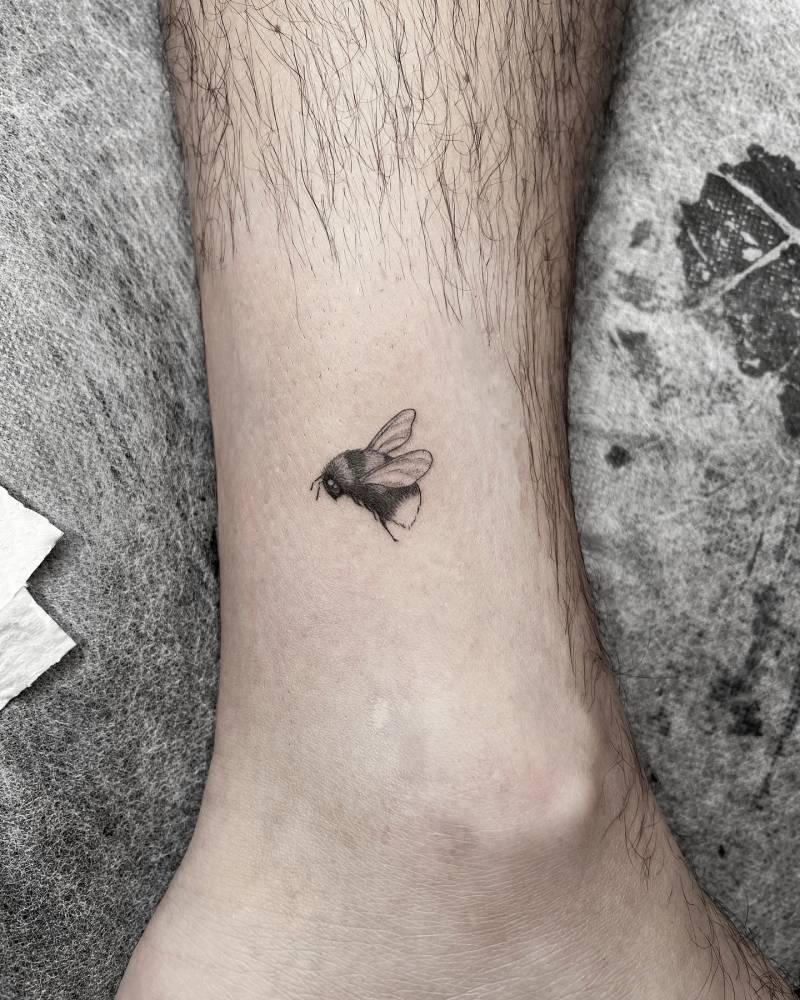 Tiny bee tattoo in illustrative style located on the ankle.