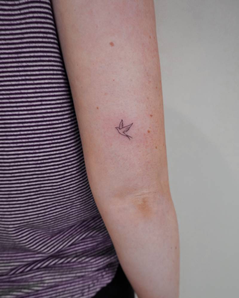 Tiny minimalist swallow tattoo located on the tricep.