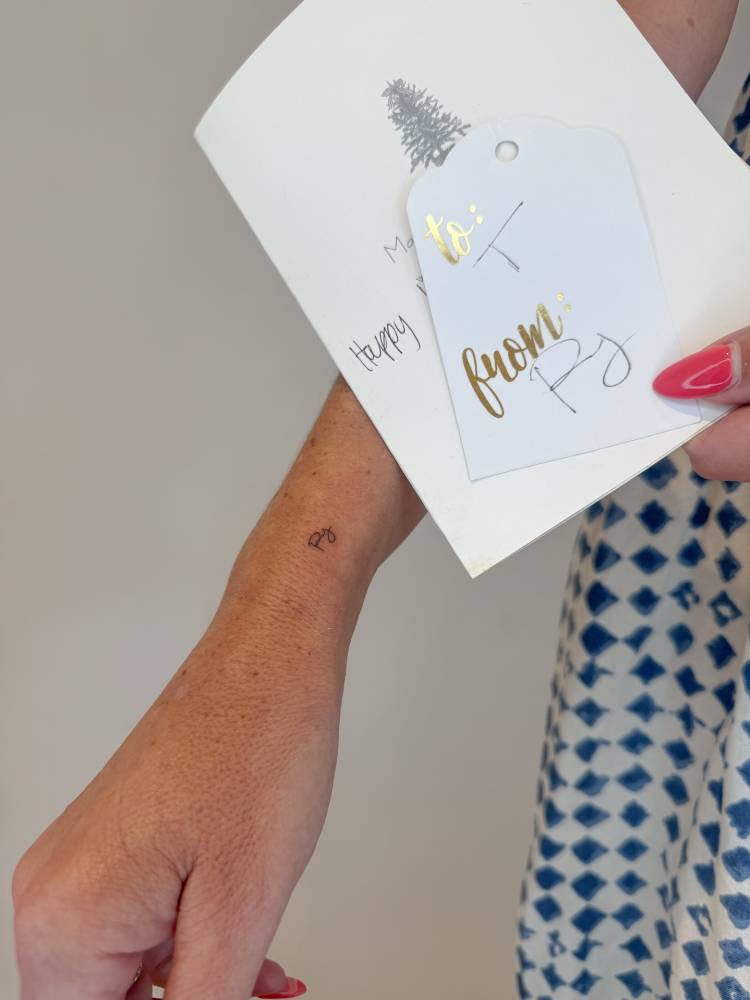 Initials tattoo in handwritten font located on the wrist.