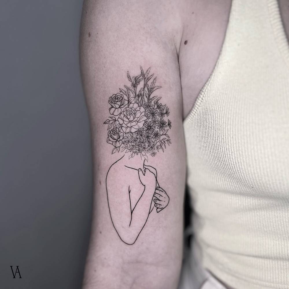 Flower head woman tattoo located on the bicep.