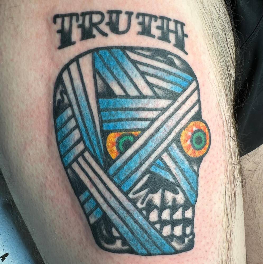 Mummy head and word "truth" tattooed on the thigh, traditional style.