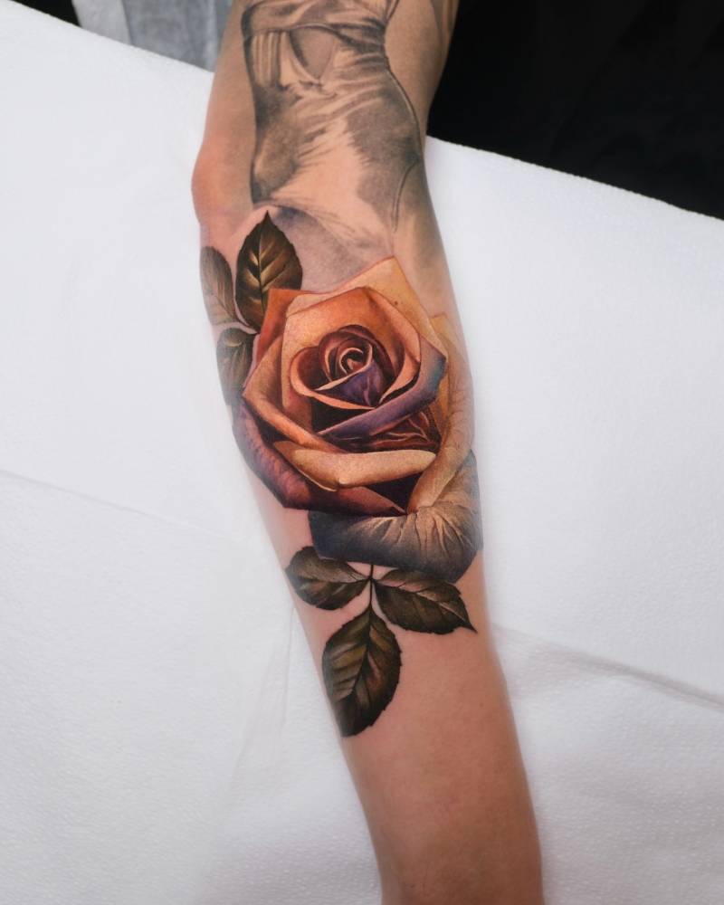Realistic style orange rose tattoo located on the forearm.