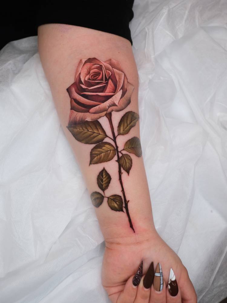 Pink rose tattoo in realistic style located on the inner forearm.