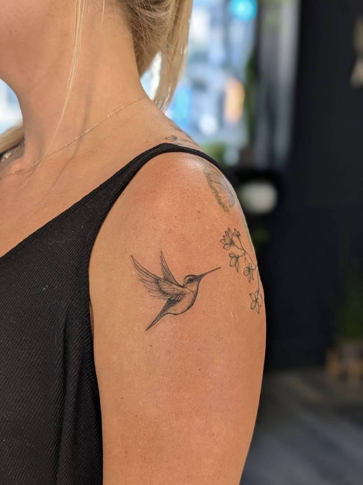 Little hummingbird tattoo located on the upper arm, illustrative style.