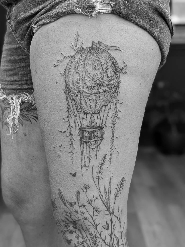 Hot air balloon tattoo located on the thigh, illustrative style.