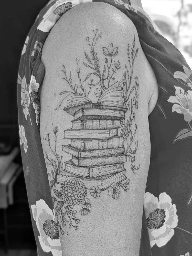 Books and flowers tattooed on the upper arm, done in illustrative style.