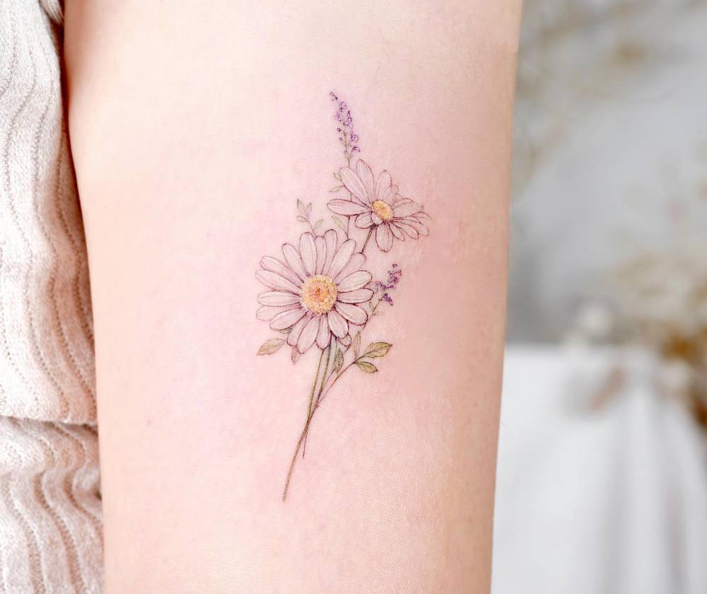 Daisies tattoo in watercolor style placed on the upper arm.