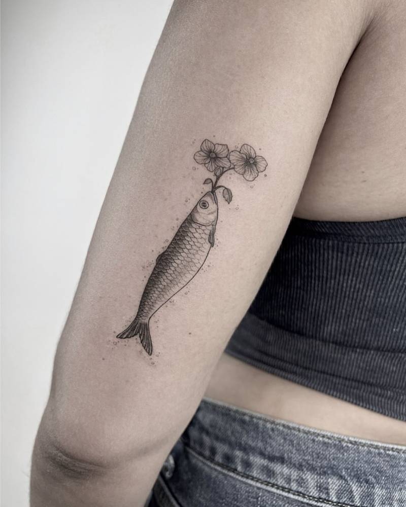 Fish and flowers tattoo located on the tricep, illustrative style.