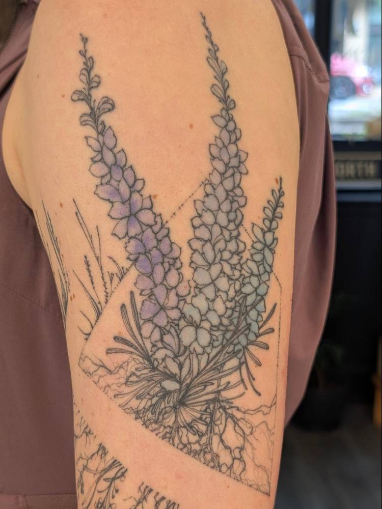 Healed lupine flowers tattooed on the upper arm, illustrative style.