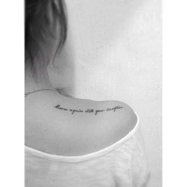 "Born again still your daughter" lettering tattoo located on the top of shoulder.