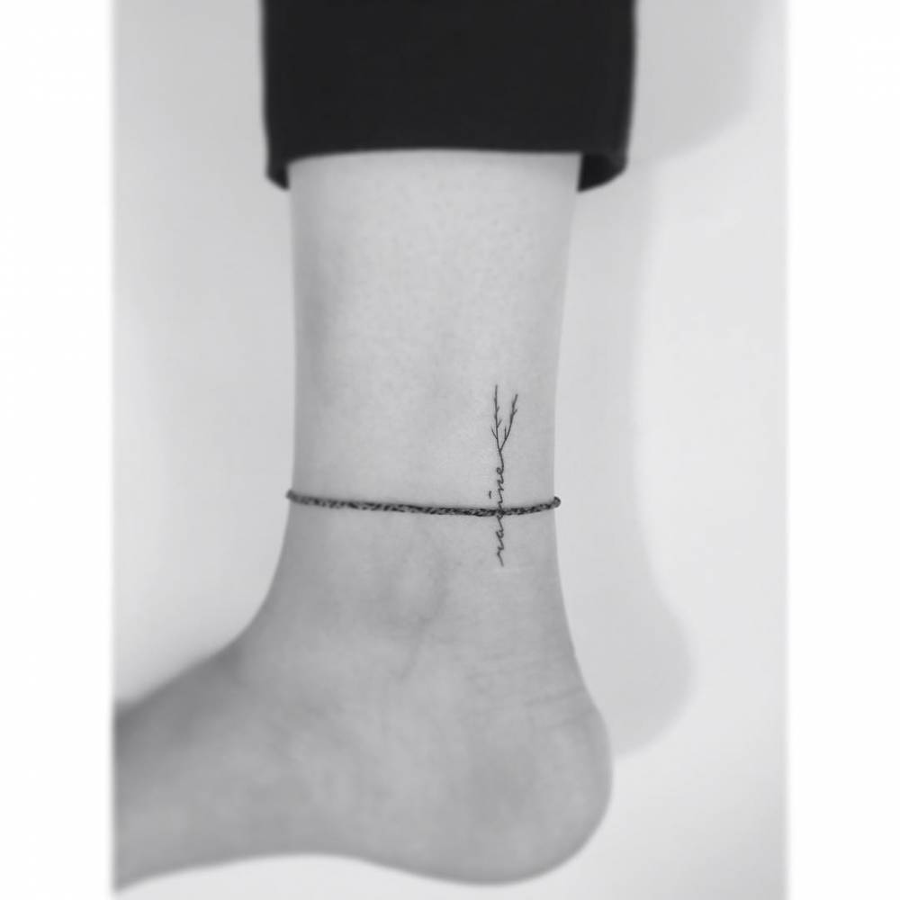 Tree branch and lettering tattoo located on the ankle.