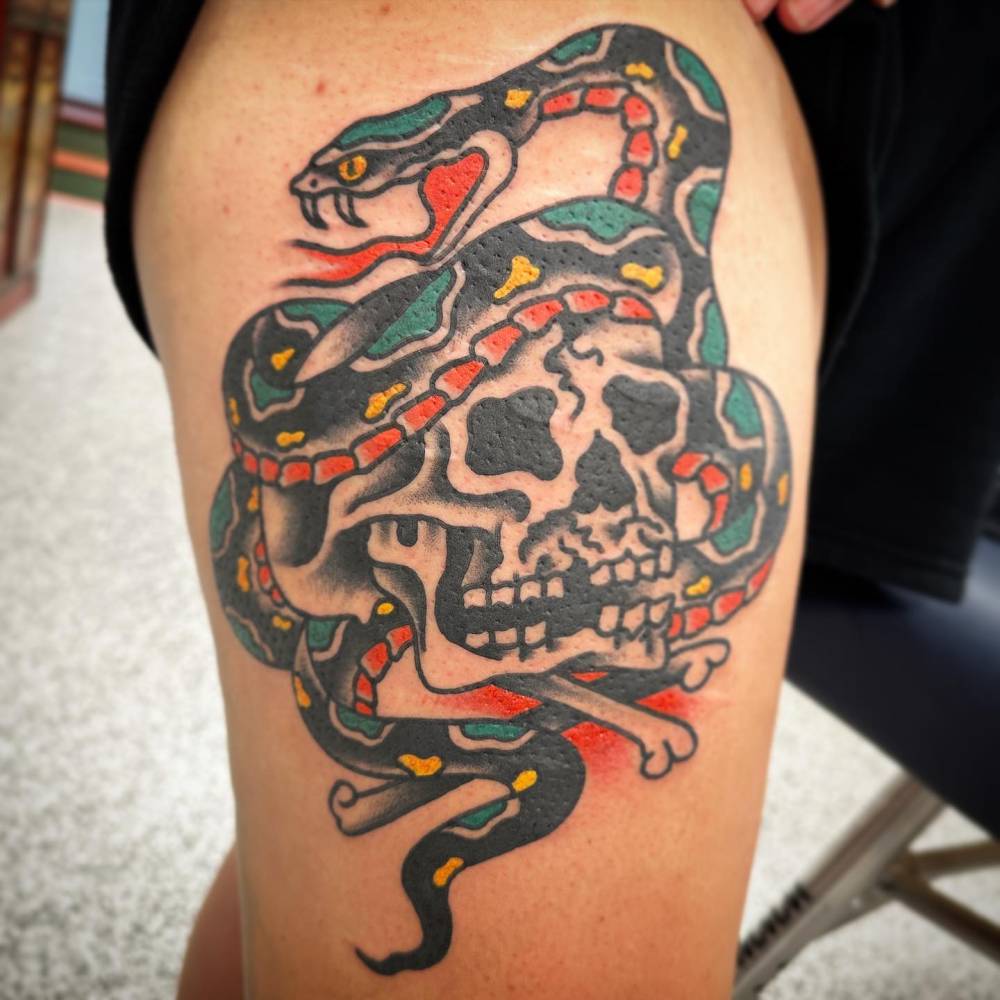 Skull and snake tattoo in traditional style located on the thigh.