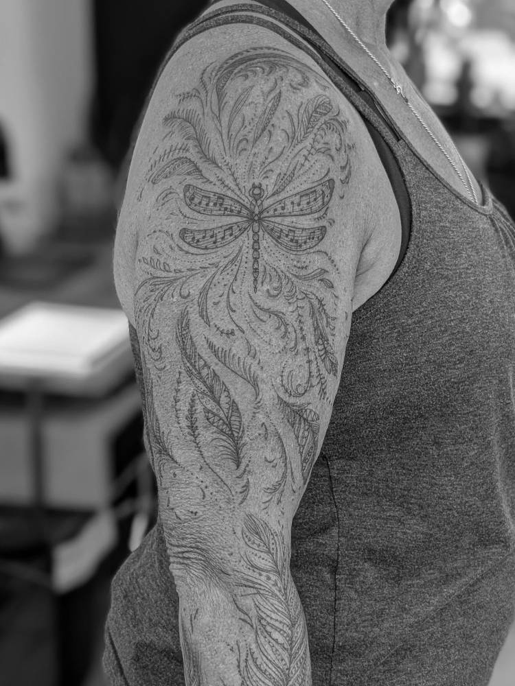 Dragonfly and feathers tattoo located on the upper arm, illustrative style.