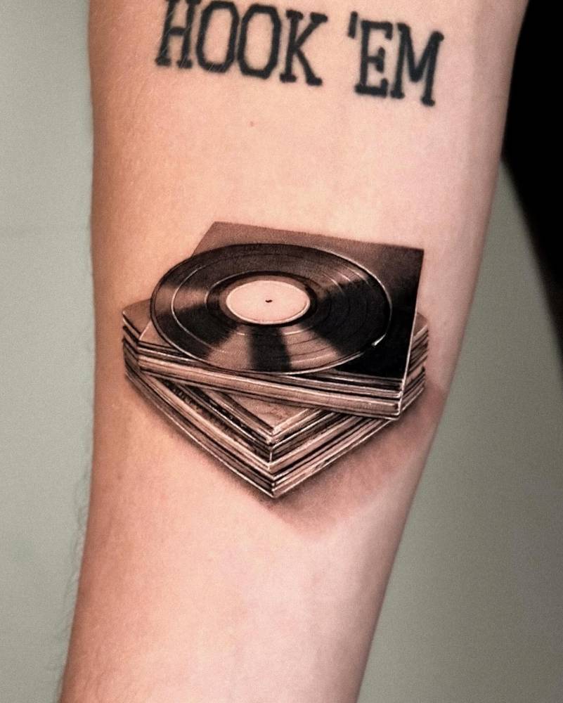 Vinyl records tattooed on the inner forearm, micro-realistic style.