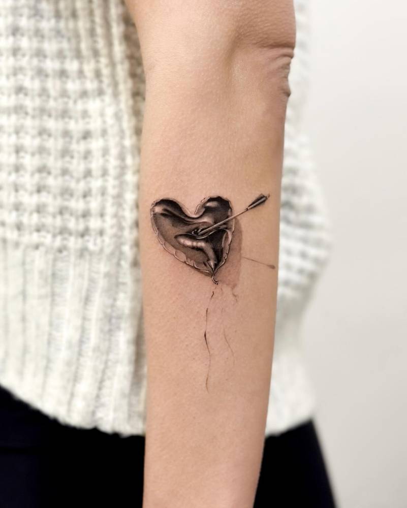 Balloon heart and arrow tattoo located on the forearm.