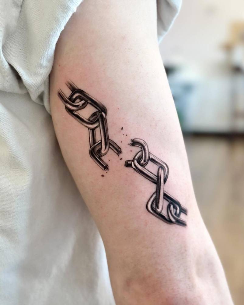 Broken chain tattoo in black and grey style located on the tricep.