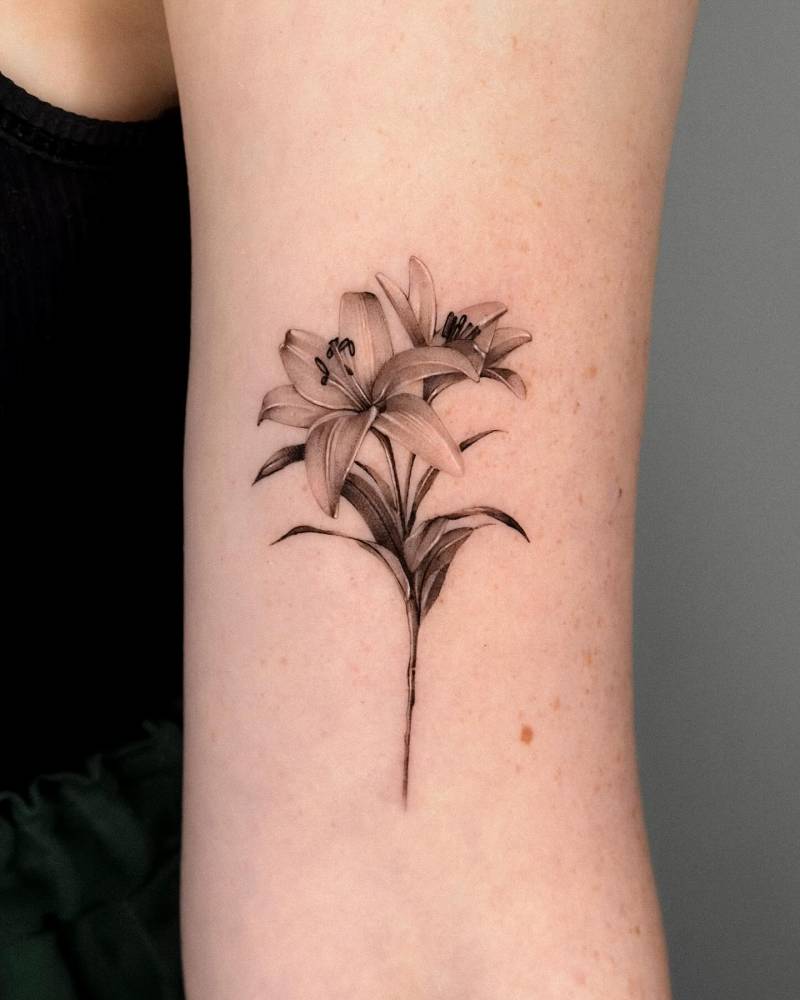 Lily flowers tattooed on the bicep, done in micro-realistic style.