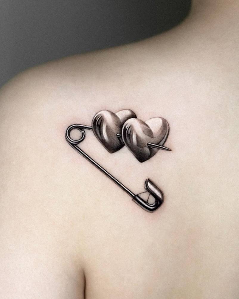 Safety pin and hearts tattoo located on the shoulder blade.