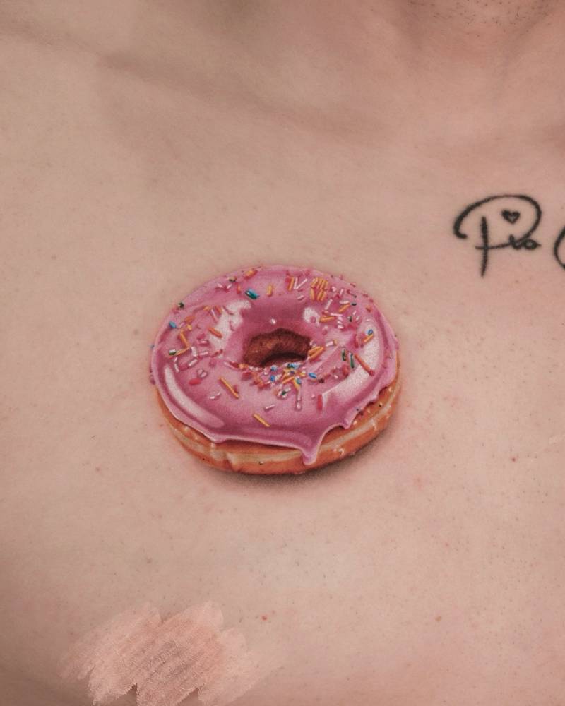 Micro-realistic style donut tattoo located on the chest.