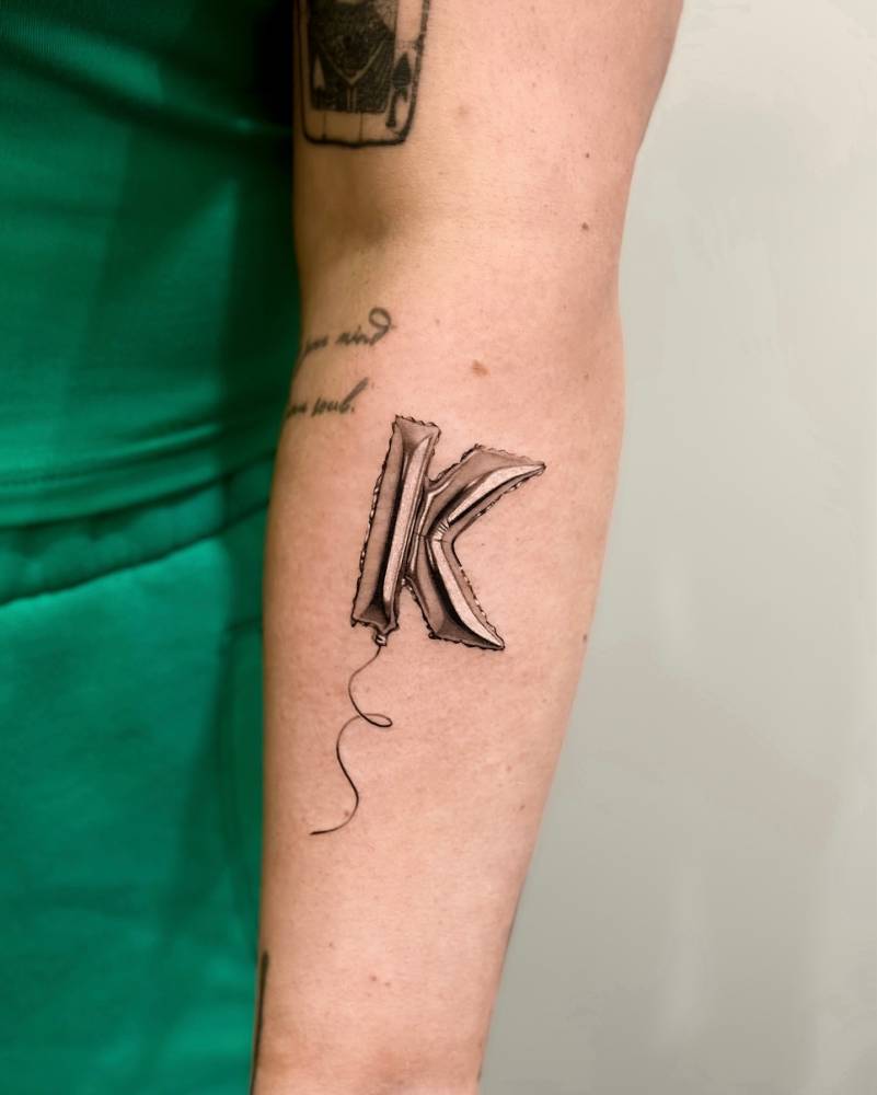 Letter "K" balloon tattoo located on the forearm.