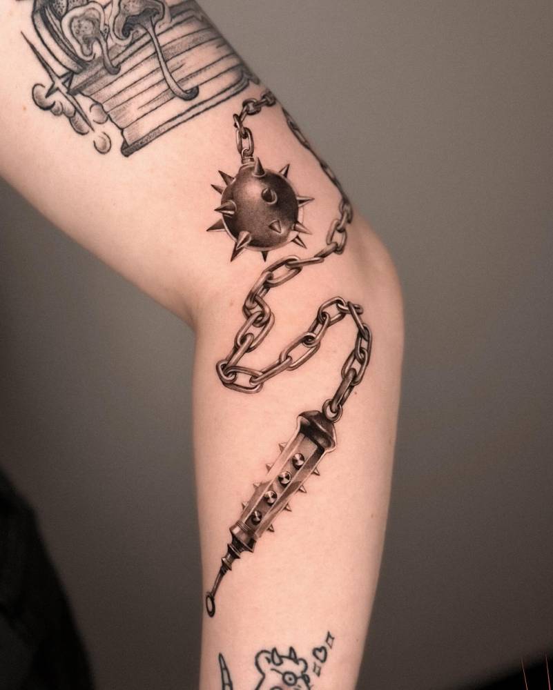 Black and grey flail tattoo located on the elbow.