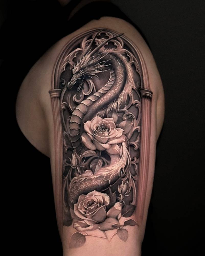 Dragon and roses tattoo in black and grey style located on the upper arm.