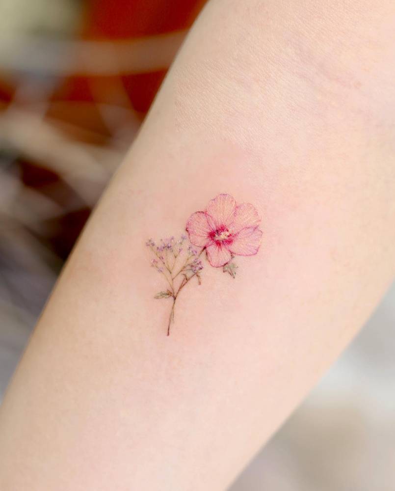 Hibiscus flower tattooed on the inner forearm, watercolor style.