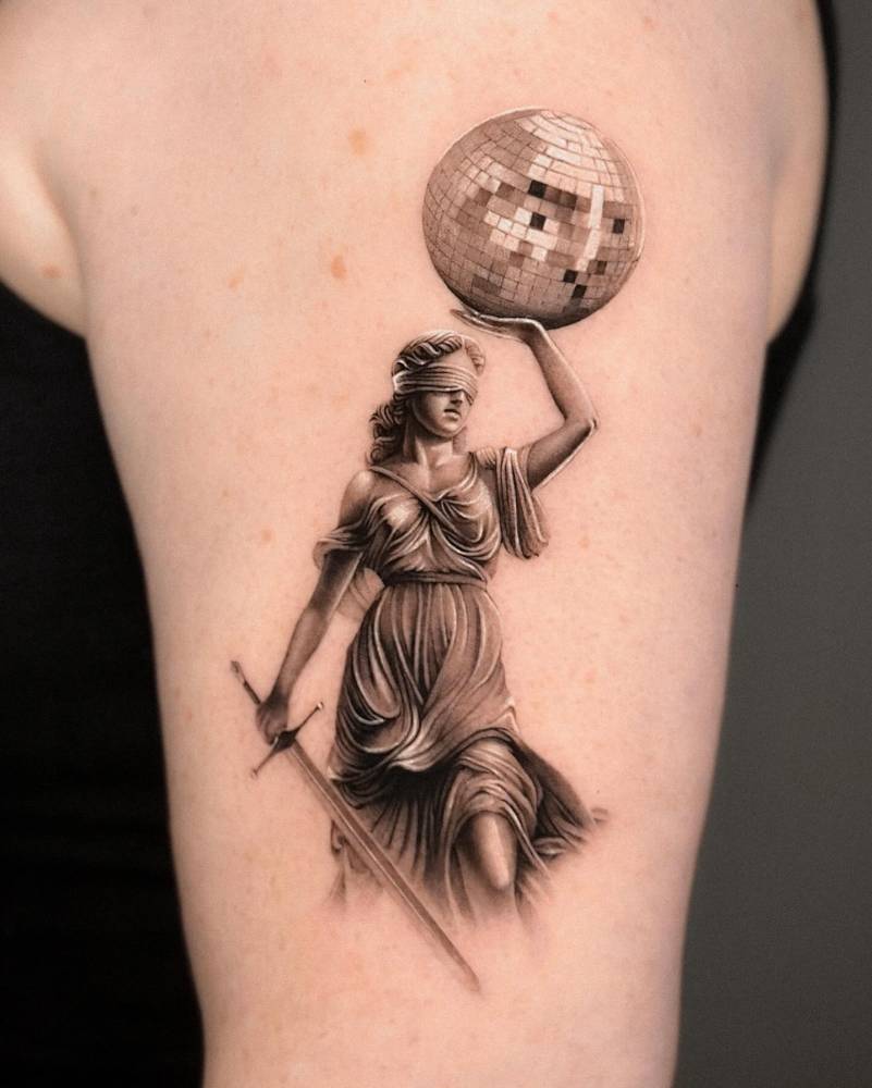 Lady Justice holding a disco ball tattoo located on the upper arm.