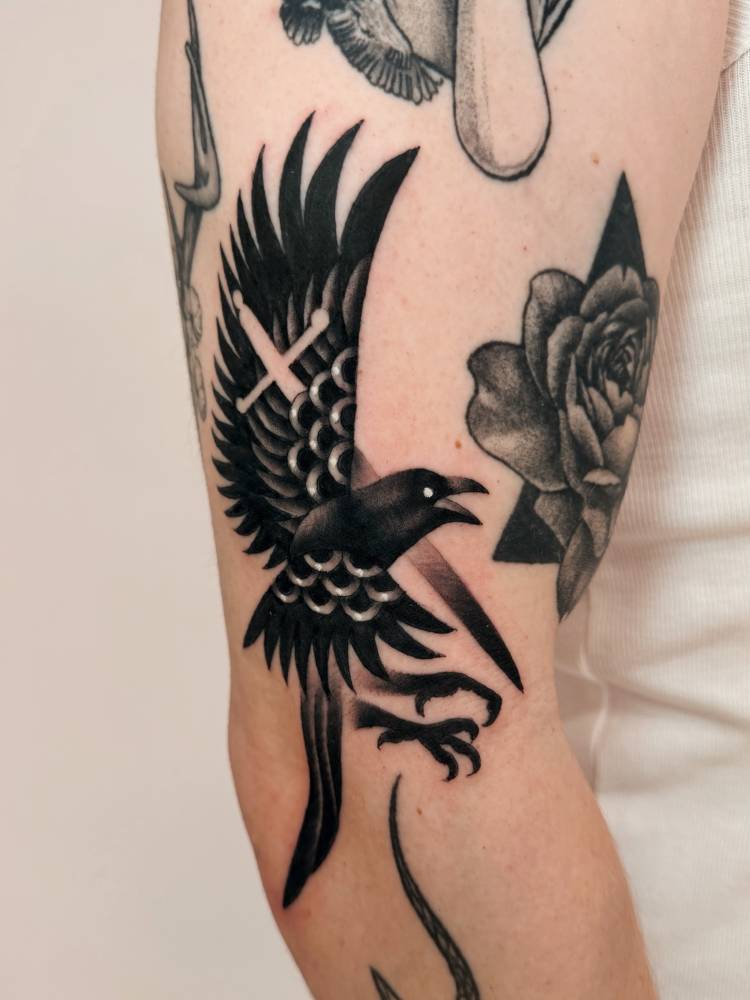 Raven and sword tattoo located on the upper arm, blackwork style.