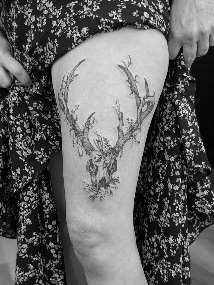 Deer skull tattoo located on the thigh, illustrative style.