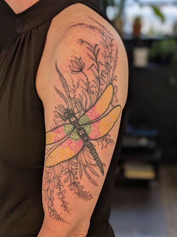 Fresh freehand floral and healed dragonfly tattoo located on the upper arm.