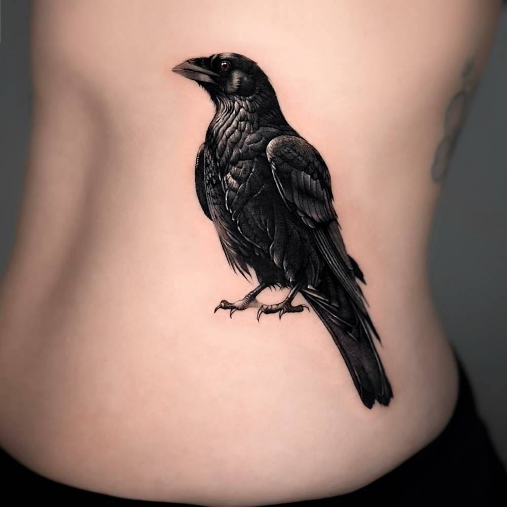 Raven tattoo in black and grey style located on the waist.