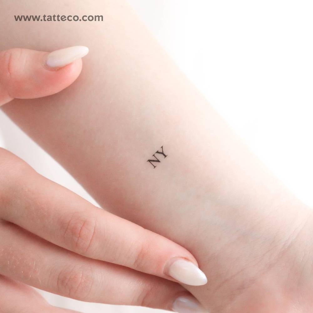 Small "NY" temporary lettering tattoo located on the wrist.