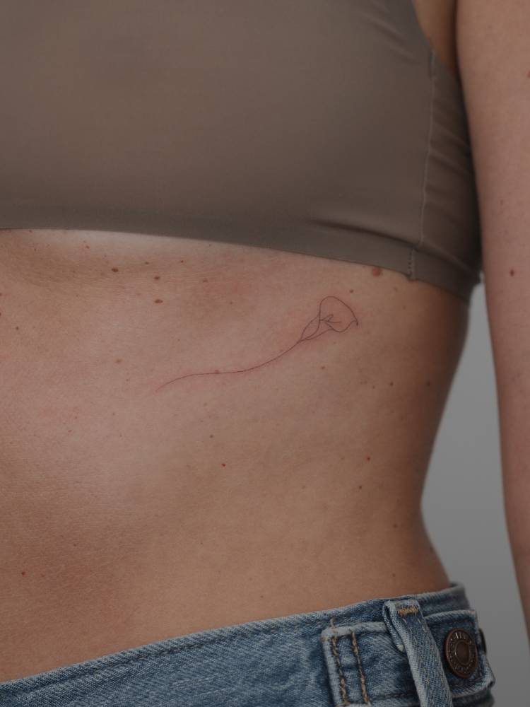 Calla lily flower tattooed on the rib, fine line style.