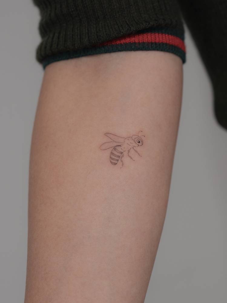 Little bee tattoo placed on the inner forearm, fine line style.