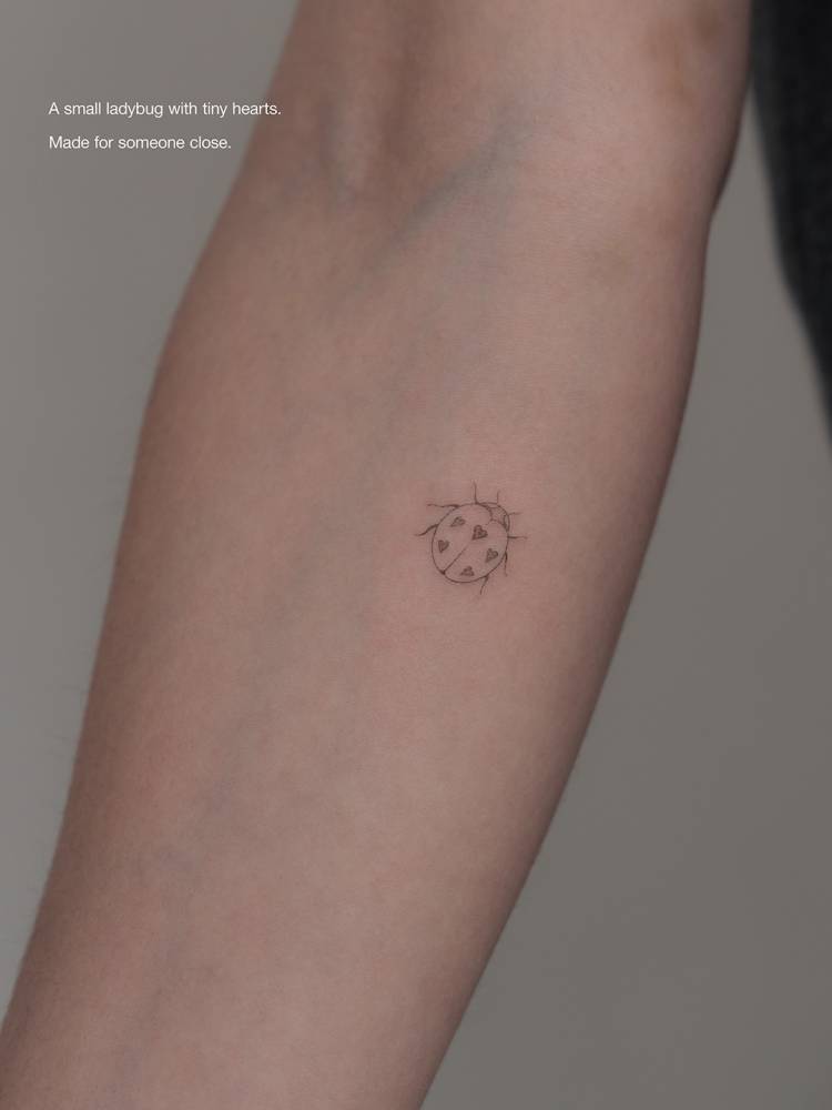Ladybug tattoo in fine line style located on the inner forearm.
