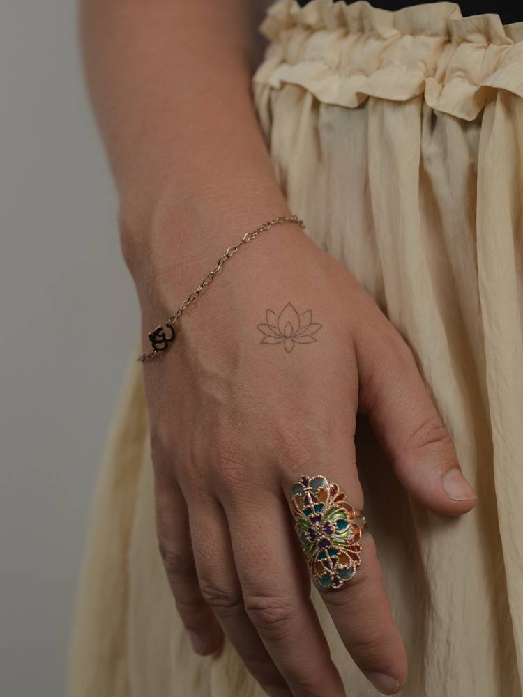 Fine line style lotus flower tattoo located on the hand.