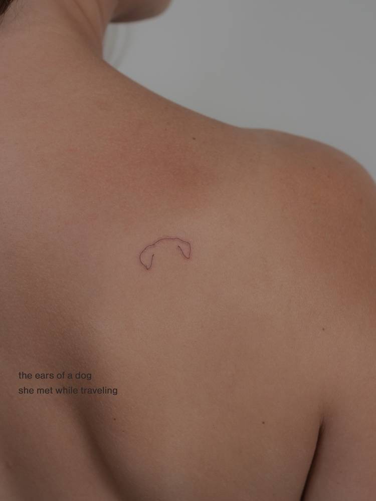 Tiny minimalist dog ears tattoo located on the shoulder blade.