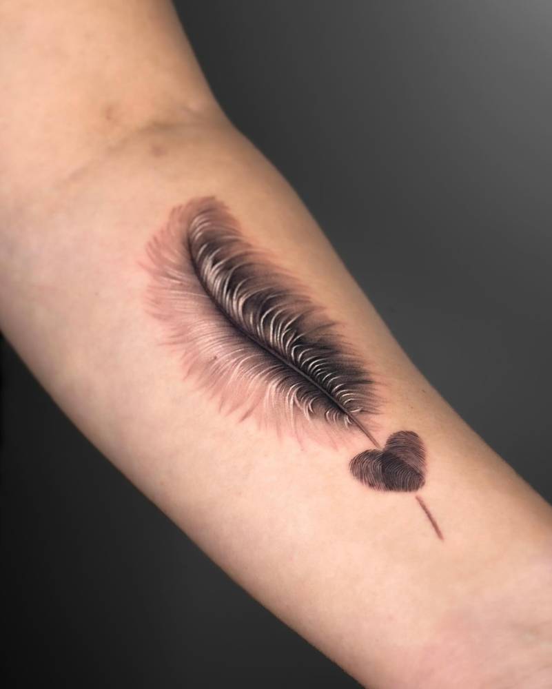 Feather and fingerprint heart tattoo located on the inner forearm.