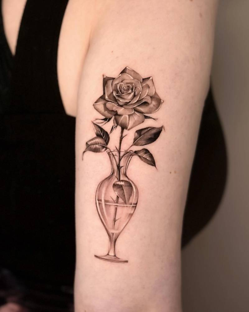 Rose in a glass bottle tattooed on the tricep, black and grey style.