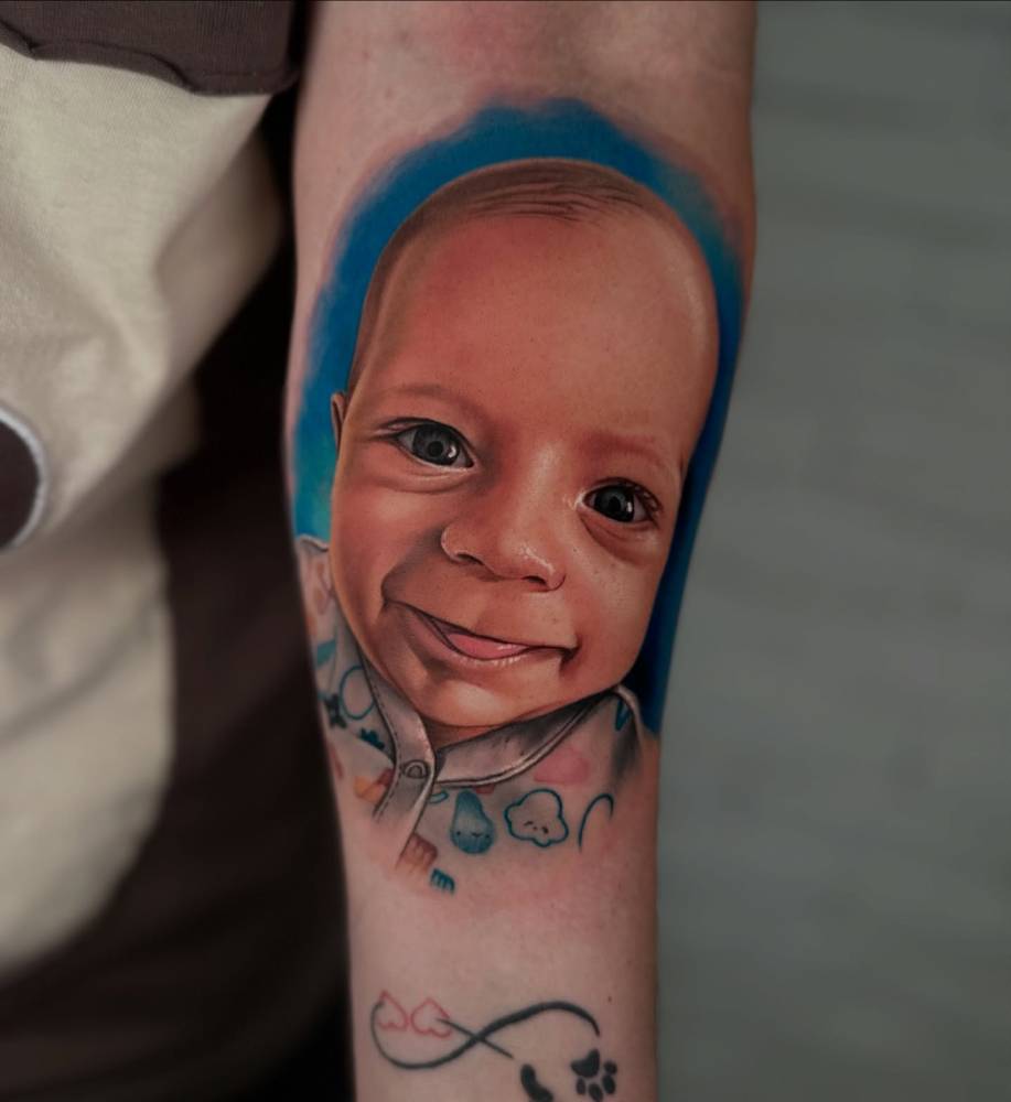Baby portrait tattoo located on the inner forearm, realistic style.